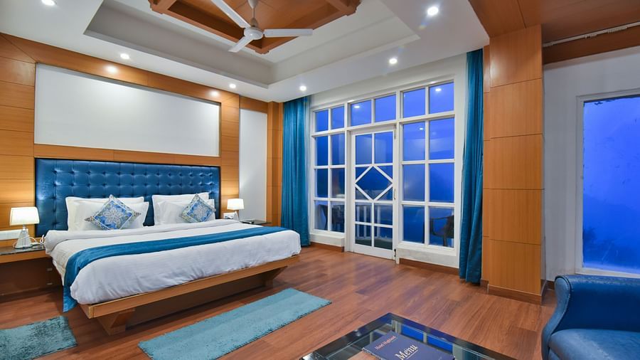 A large bed placed in front of the sofas in Luxury Room with Balcony at DLS Highland Resort and Spa, Mussoorie.